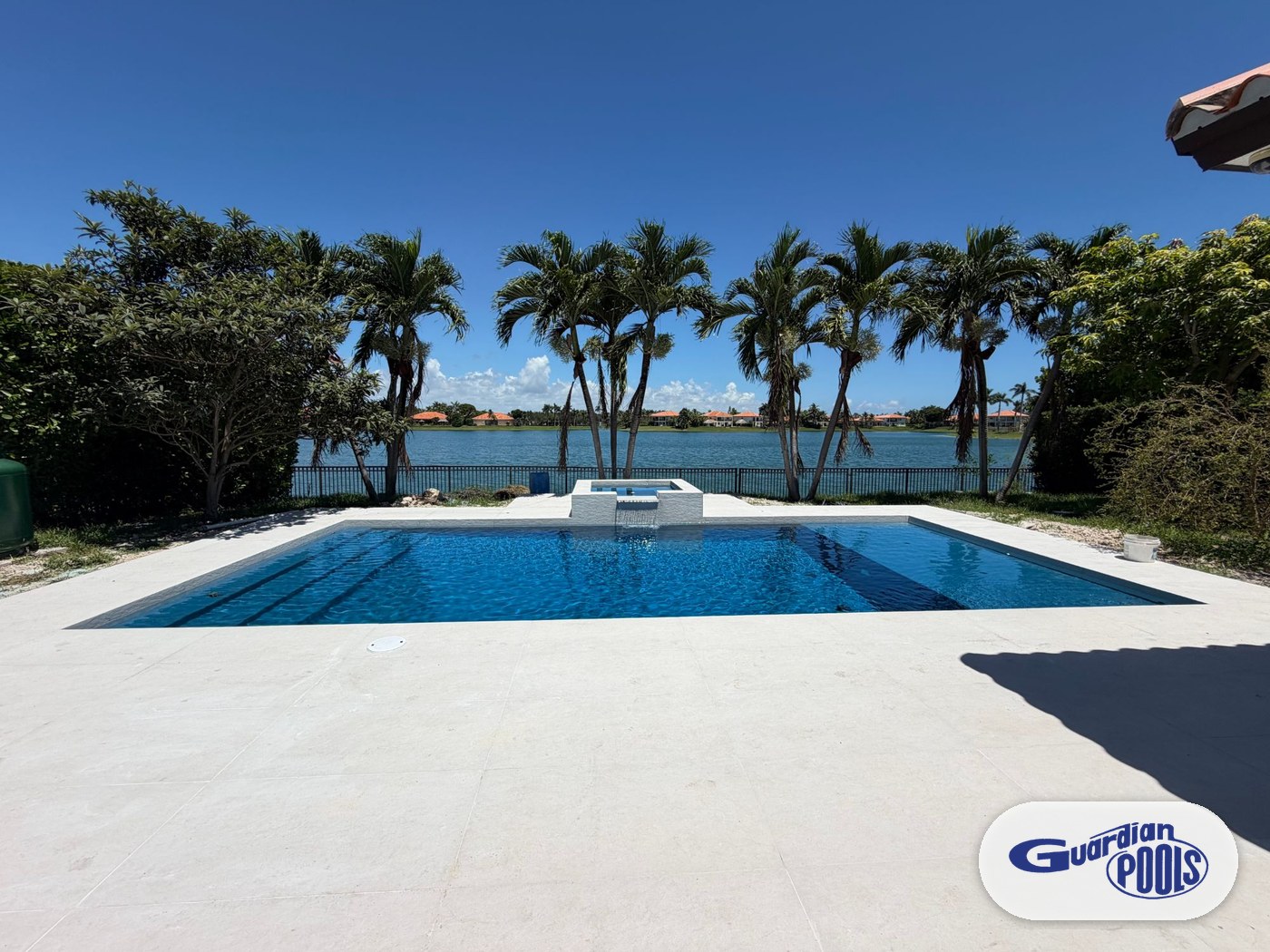 Finished rectangular pool with raised spa, spillway, and white paver deck on a lakefront property after a full remodel