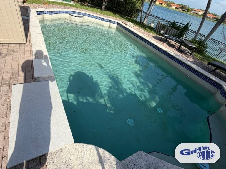 Round pool with worn tan pavers and dated blue mosaic tile before a full remodel