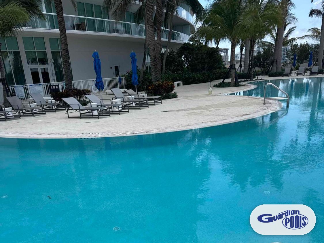 Resurfaced highrise community pool in Pompano Beach with curved deck, lounge chairs, and palm trees